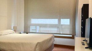 Een moderne slaapkamer met een groot bed, een nachtkastje, een televisie en een raam met zonwering.