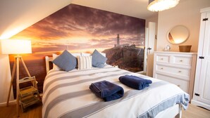 Una camera da letto con un letto, un comodino, una cassettiera e un affresco raffigurante un tramonto su un faro.