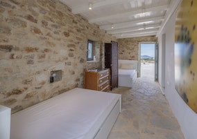 Quarto com paredes de pedra, penteadeira de madeira, cama e vista para o exterior.