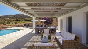 Una zona de estar al aire libre techada, con suelo de piedra, mobiliario de mimbre y piscina.