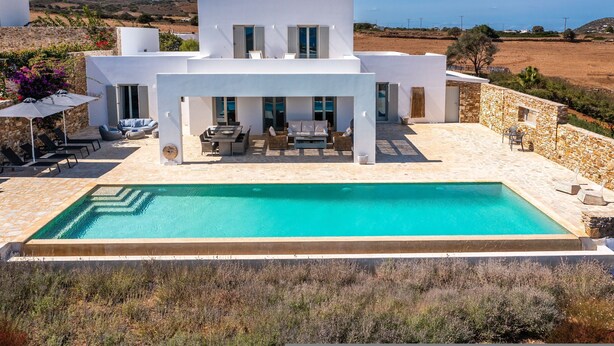 Una villa moderna con piscina, mobiliario exterior y vistas del paisaje circundante.