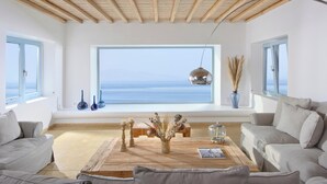Un salon spacieux doté d’une grande fenêtre donnant sur la mer, de poutres apparentes en bois au plafond et d’un coin salon confortable.