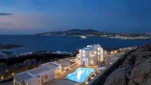 Un hôtel en bord de mer doté d’une piscine, d’une architecture blanche et offrant une vue sur la mer et les lumières lointaines de la ville.