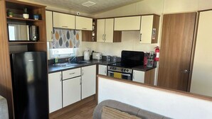 A compact kitchen with a refrigerator, stove, microwave, and sink. - 3 Bedroom Caravan - Pets, Parking, Pool Access (Cirencester)
