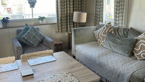 A cozy living room with a grey sofa, a matching armchair, and a wooden coffee table. - 3 Bedroom Caravan - Pets, Parking, Pool Access (Cirencester)