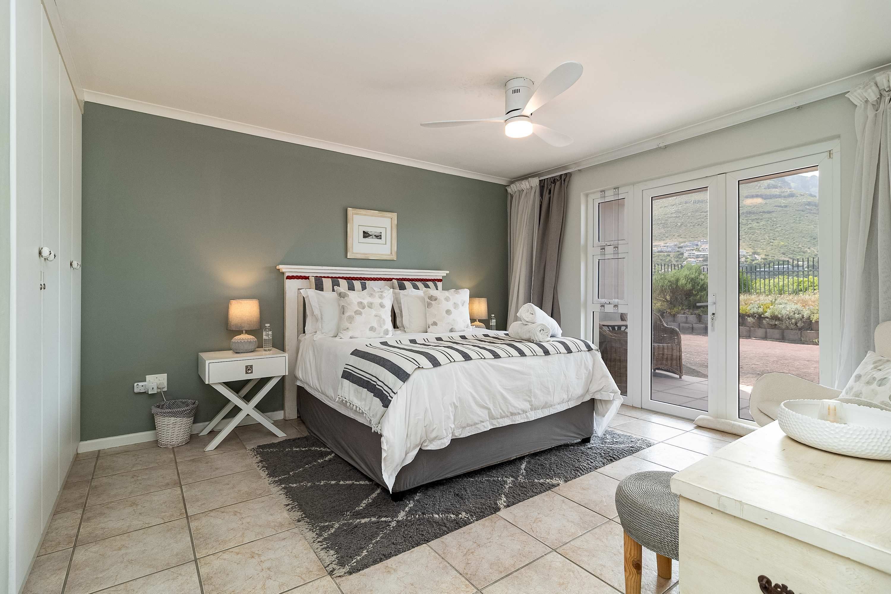 Een slaapkamer met een bed, nachtkastjes, een plafondventilator en uitzicht door een schuifglazen deur.