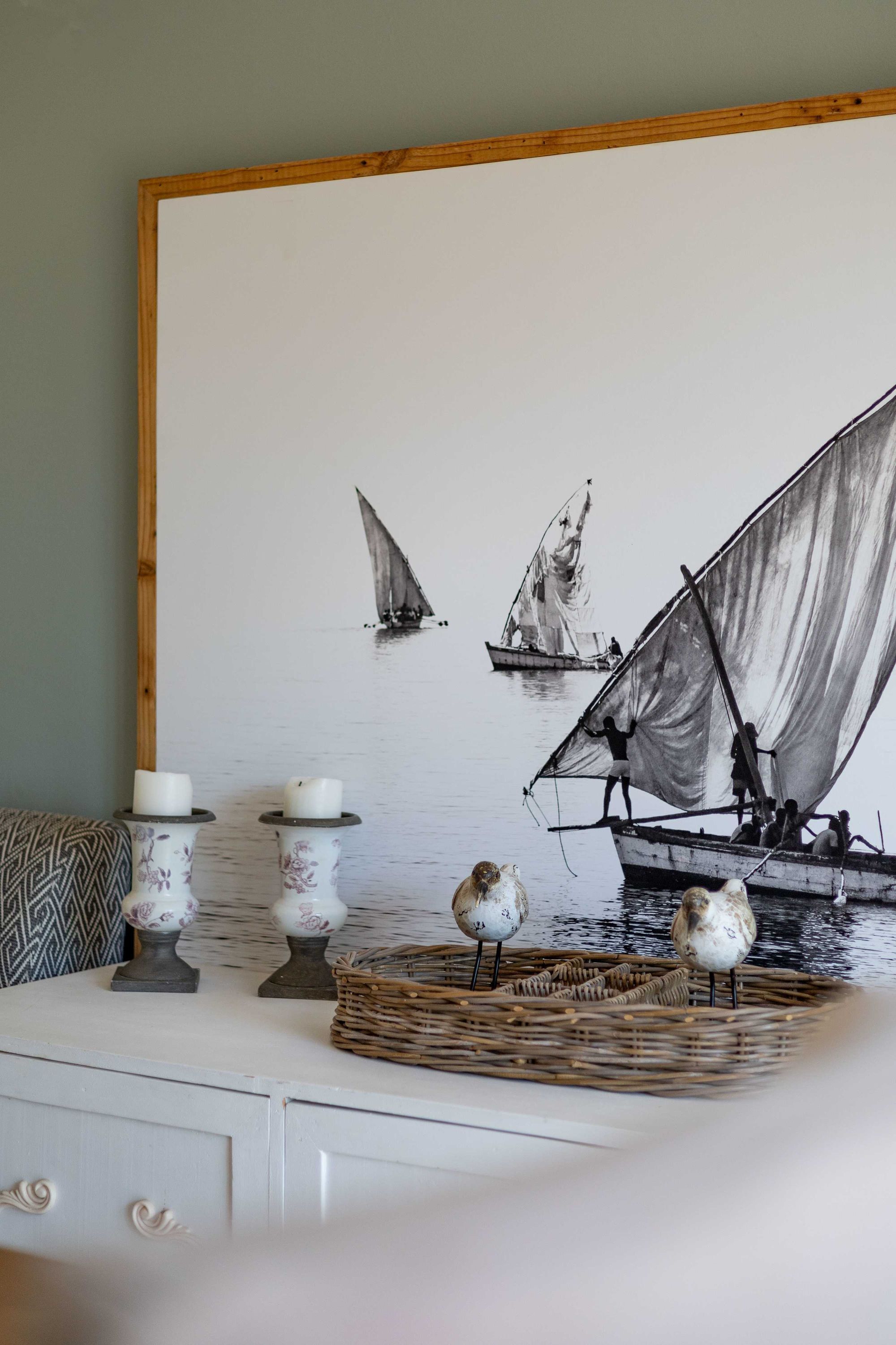 A room with a large wall painting of sailboats, a white dresser with decorative items, and a patterned throw pillow.