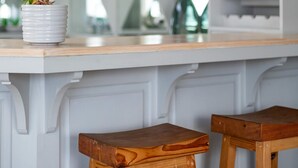 Una encimera de cocina con una planta en maceta, taburetes de madera y un armario blanco con estantes.