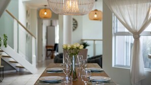 Un comedor con una mesa dispuesta para seis comensales, un jarrón de rosas blancas e iluminación colgante.