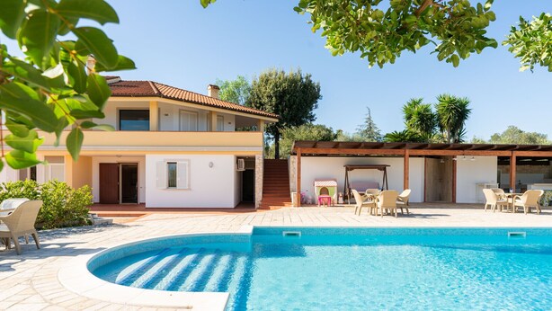 A two-story house with a swimming pool, outdoor seating, and a covered patio area.