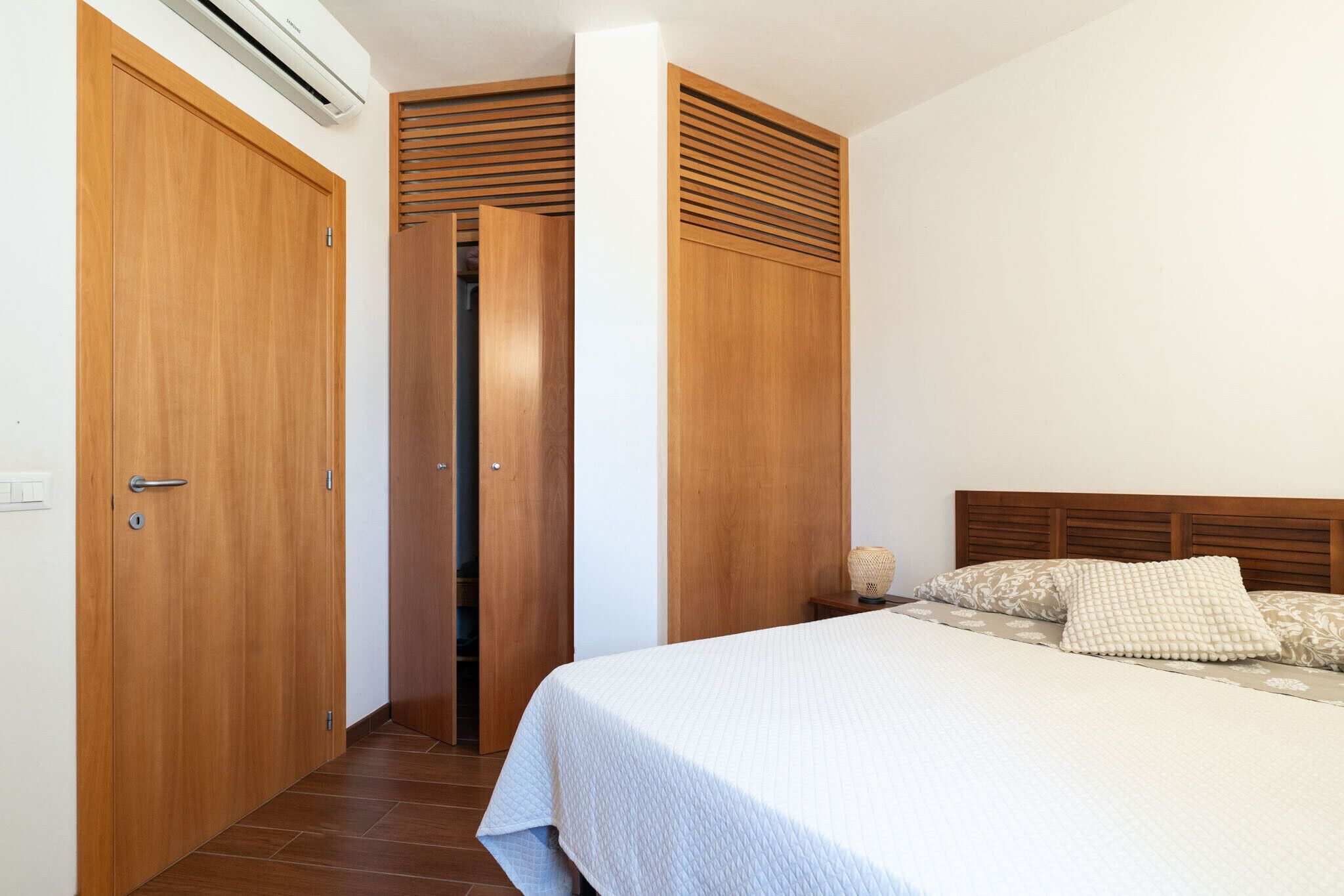 Een slaapkamer met een bed, een houten garderobe en een airconditioning.