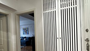 Een gang met een houten visgraatvloer, een witte deur met een sleutelgat, en een witte muur met een ventilatierooster.