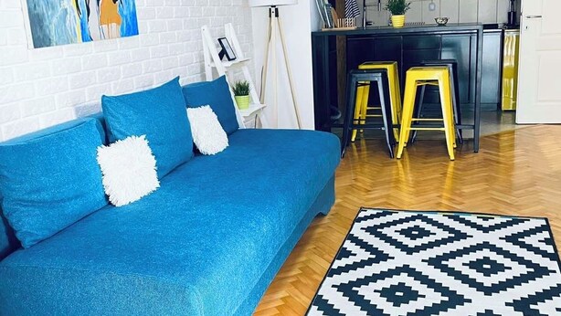 Een moderne woonkamer met een blauwe bank, een kamerbreed tapijt en een keuken met krukjes.