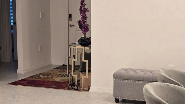 A living room with a grey sofa, a small table with a purple orchid, and a door in the background. - Home away from Home (Port St. Lucie)