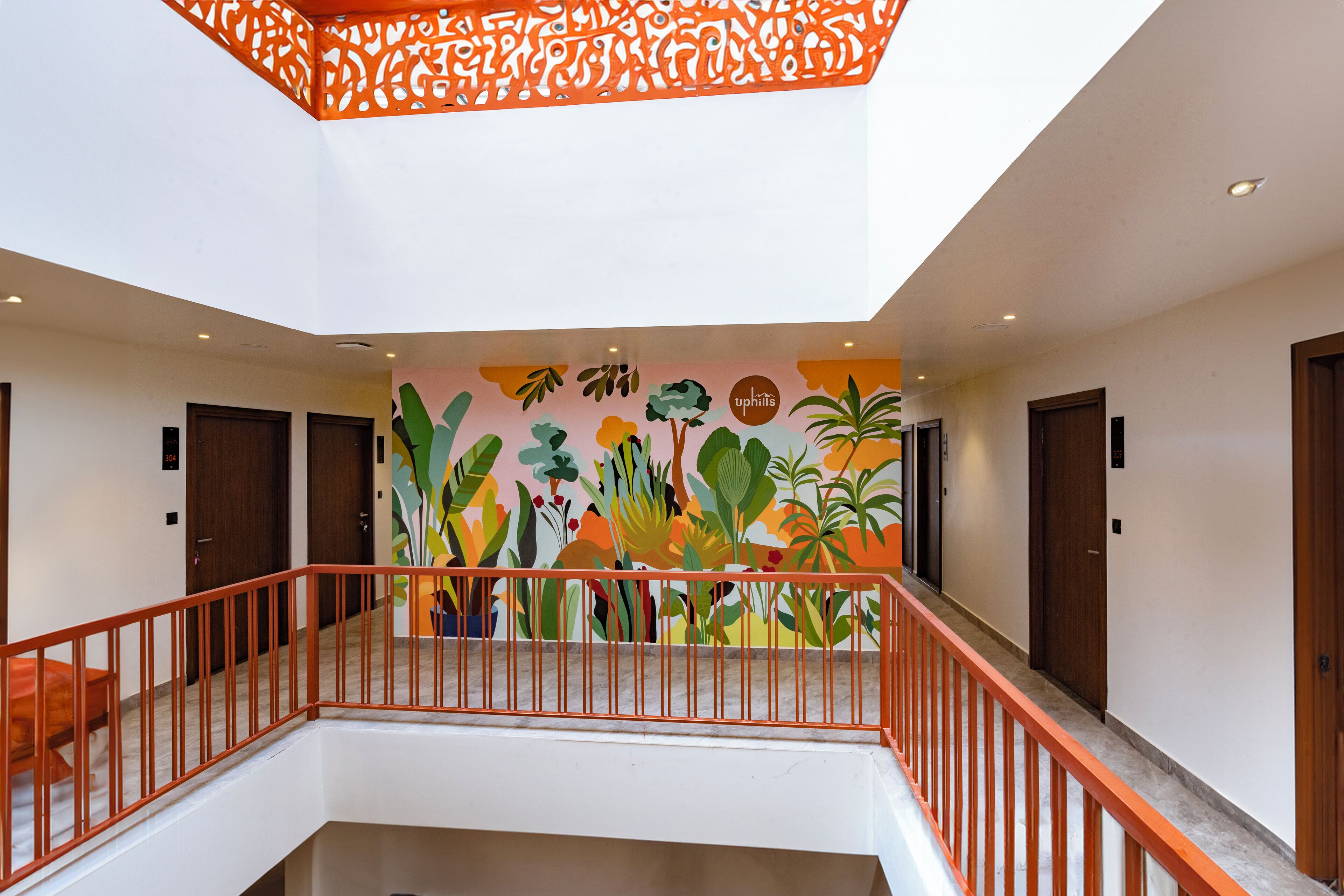 Um saguão de hotel com um mural colorido, um corrimão vermelho e uma escadaria que leva a um andar superior.