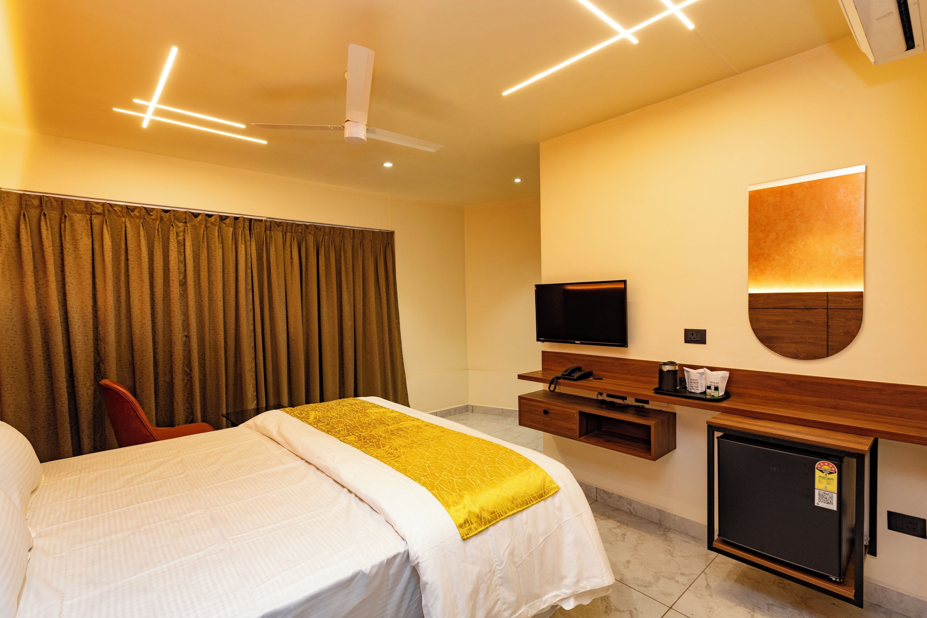 Una habitación de hotel con una cama, televisión, escritorio con computadora y un refrigerador pequeño.