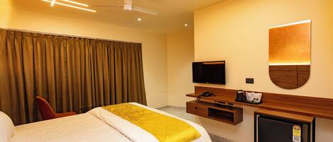 Una habitación de hotel con una cama, televisión, escritorio con computadora y un refrigerador pequeño.
