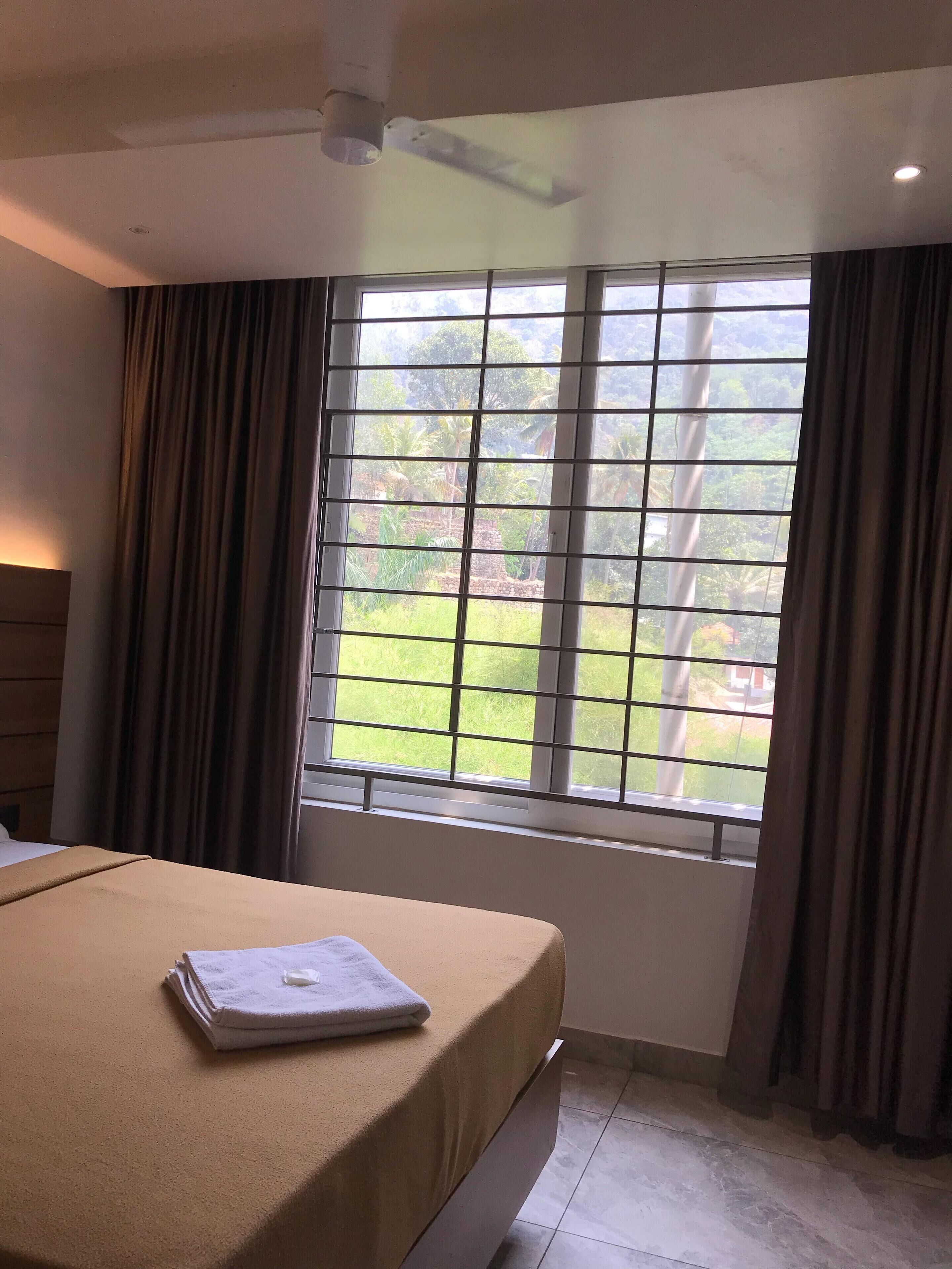 Quarto de hotel com cama, janela com cortinas e ventoinha no teto.