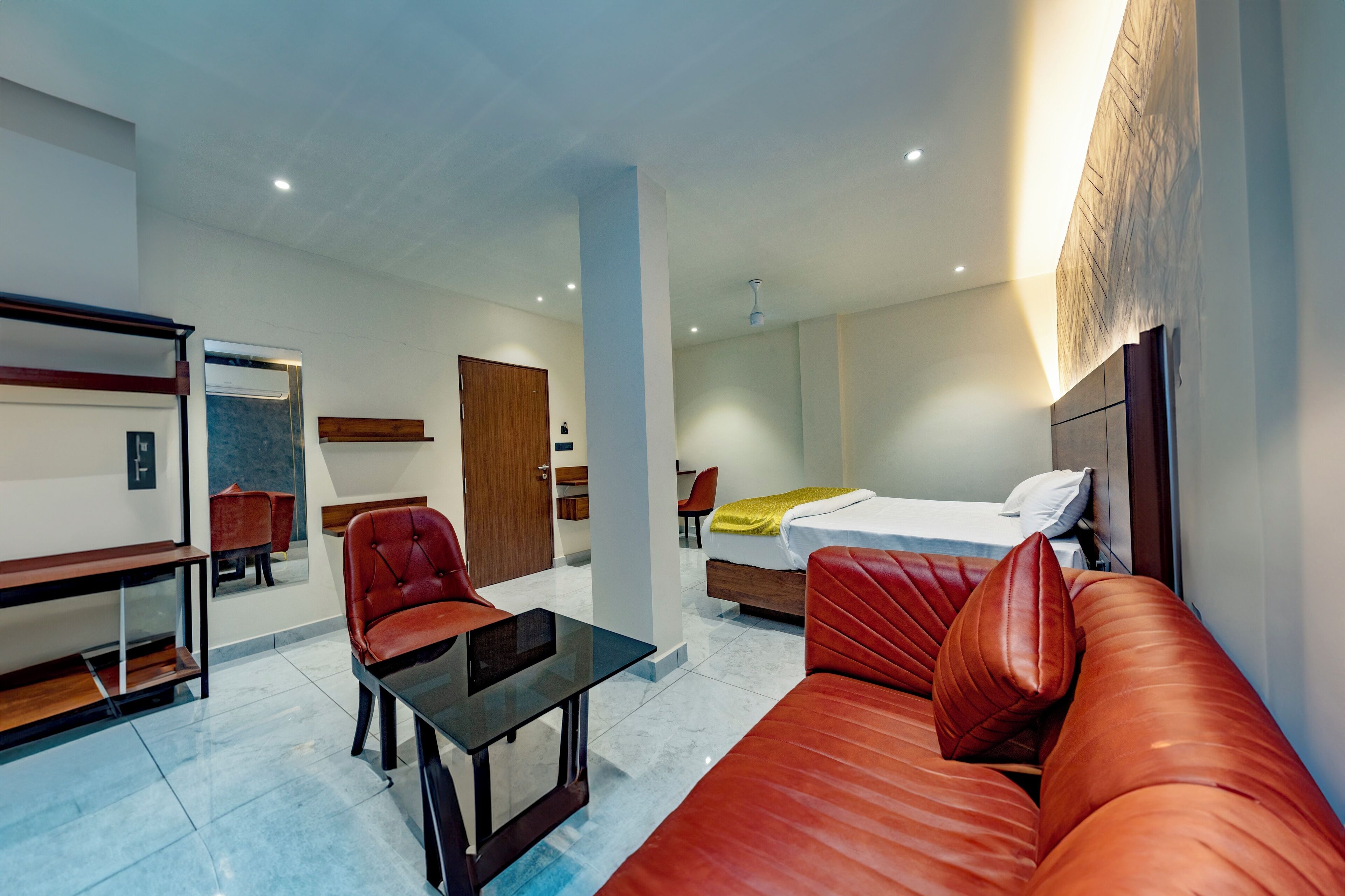 Habitación de hotel con cama, sofá de cuero rojo, mesa de centro de vidrio, escritorio de madera y una silla.