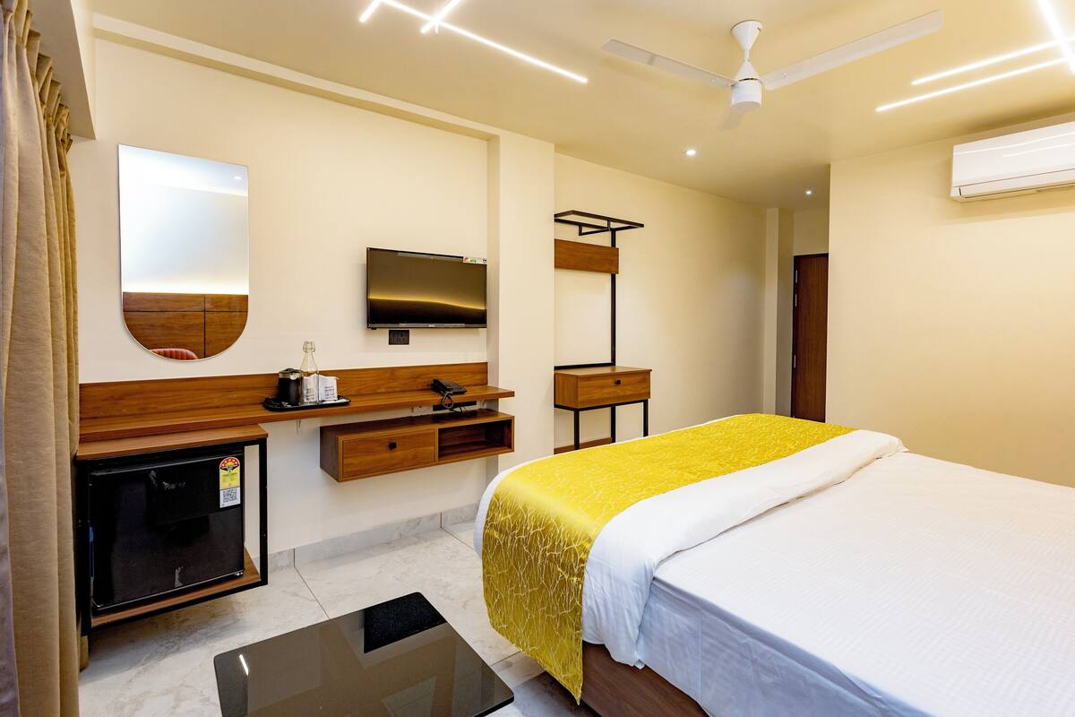 A hotel room with a bed, a TV, a ceiling fan, a small table, a mirror, and a wall-mounted air conditioner.