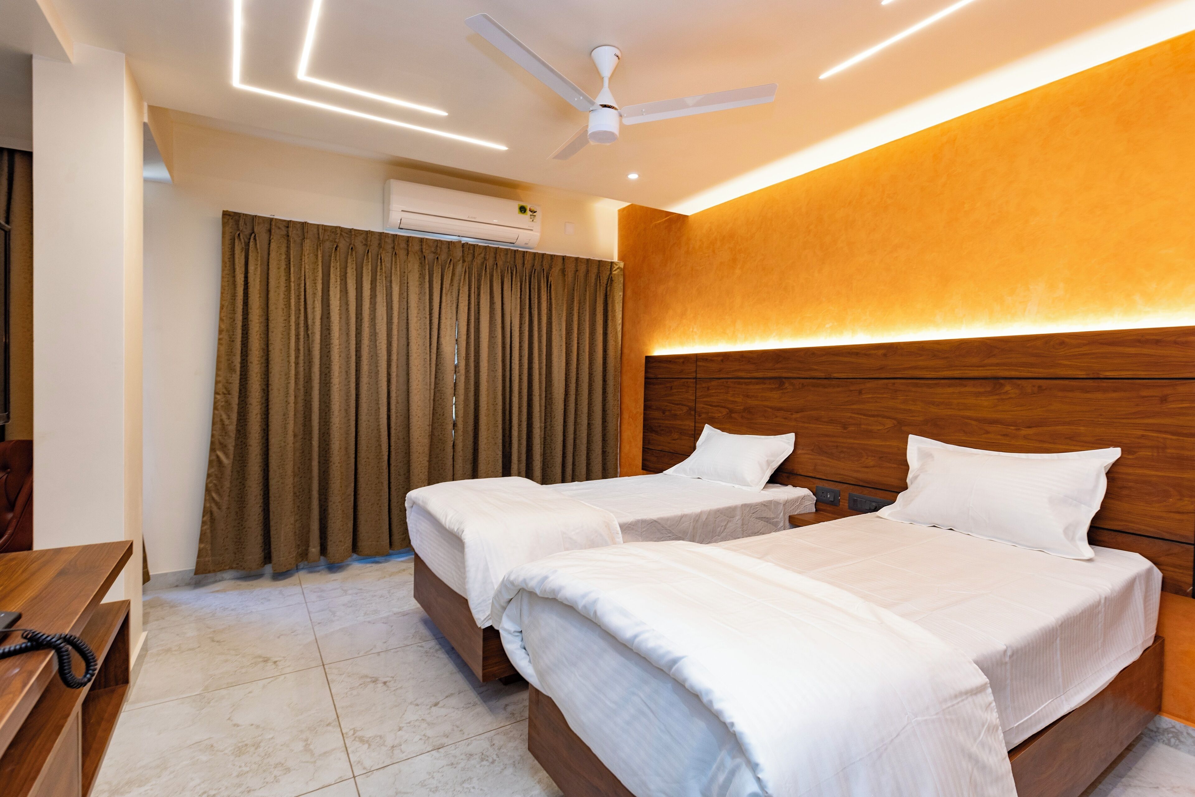 A hotel room with two beds, a ceiling fan, an air conditioning unit, and a wooden headboard.