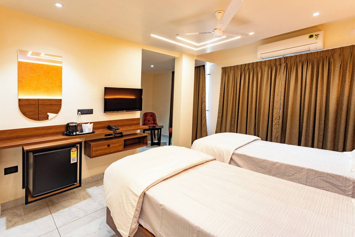 A hotel room with two beds, a desk with a computer, a television, and an air conditioning unit.