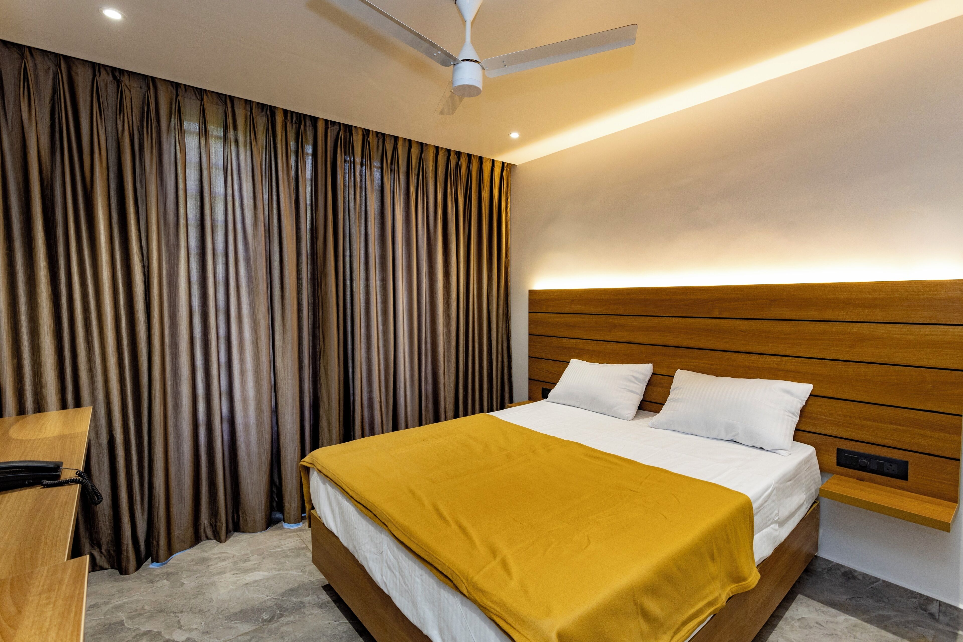 Una habitación de hotel moderna con una cama grande, un cabecero de madera, un escritorio con teléfono y un ventilador de techo.