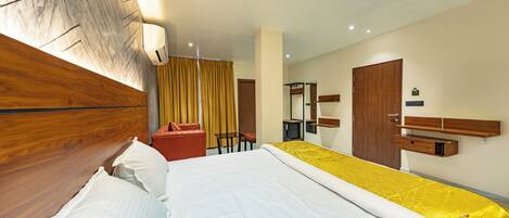 A hotel room with a wooden headboard, a bed with white linens, a yellow bedspread, a wooden nightstand, a desk, a chair, a mirror, and a wardrobe.