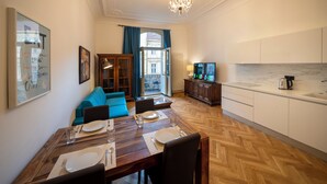 A modern living room with a dining area, wooden herringbone floor, a chandelier, and a view through a large window. - Old Town - Aparthotel 28. Října (Prague)