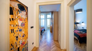 A hallway with a large, colorful painting on the left, leading to a bedroom with a bed and a desk lamp. - Old Town - Aparthotel 28. Října (Prague)