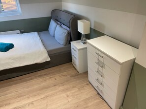 A bedroom with a bed, bedside table, lamp, and a dresser. - Ensuite near Luxmore Garden (London)