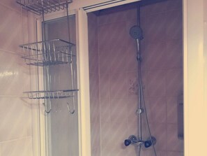 Un espacio de ducha con un estante metálico y un cabezal de ducha de mano.