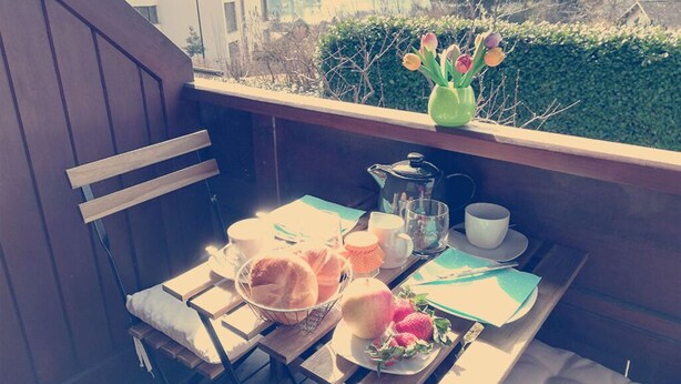 A balcony with a table set for breakfast, including bread, fruit, and a green vase with flowers. - Die Labsalerie am Wörthersee - Apartment with 1 bedroom and lake view (Pörtschach am Wörthersee)