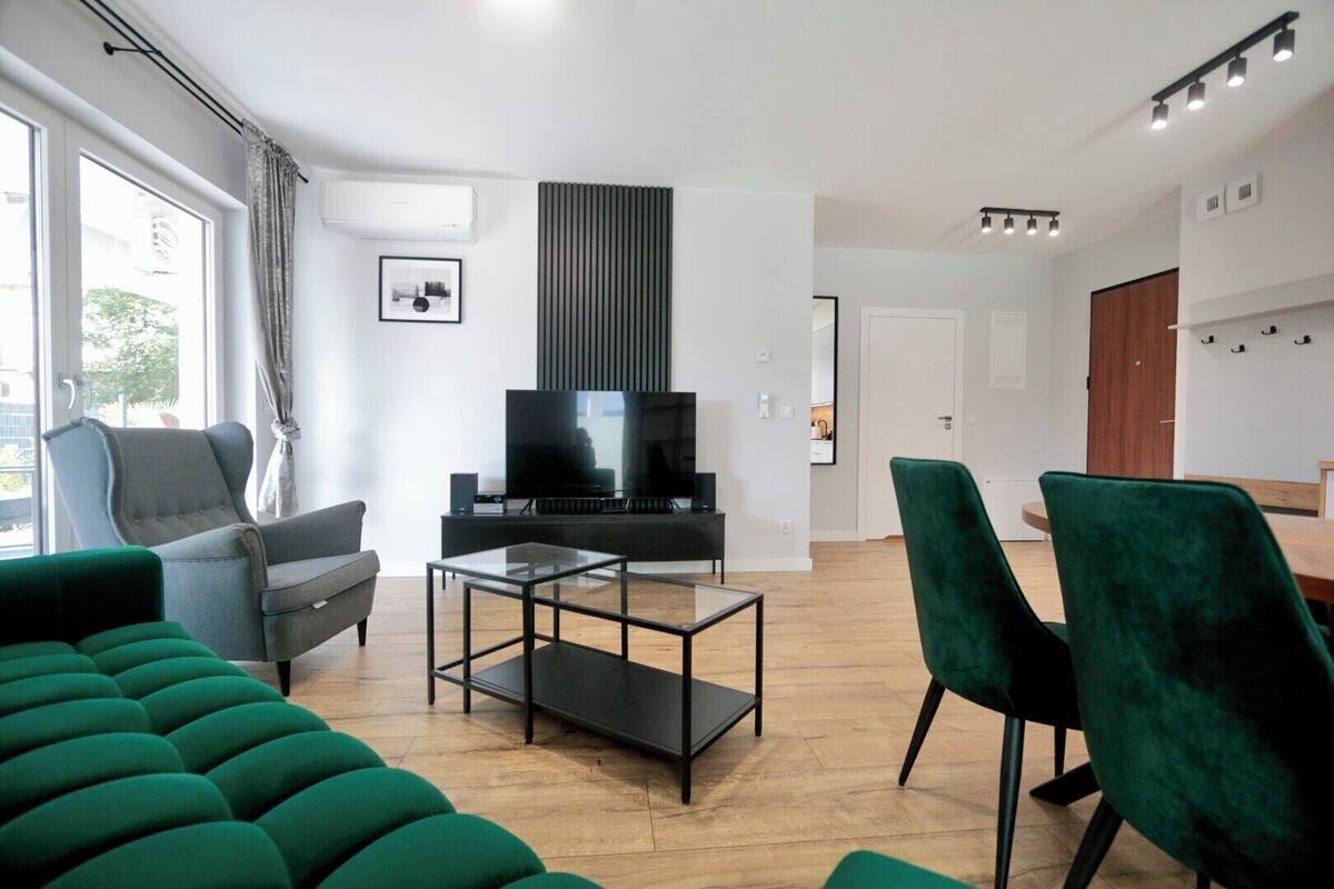 A modern living room with a flat-screen TV, a sofa, a coffee table, and a dining area with chairs.