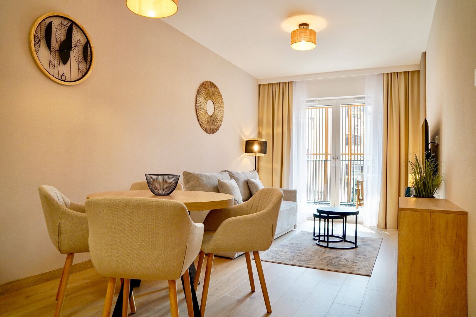 Un salon moderne avec un coin repas, comprenant une table ronde, des sièges confortables, une horloge murale décorative et une grande fenêtre avec des rideaux.