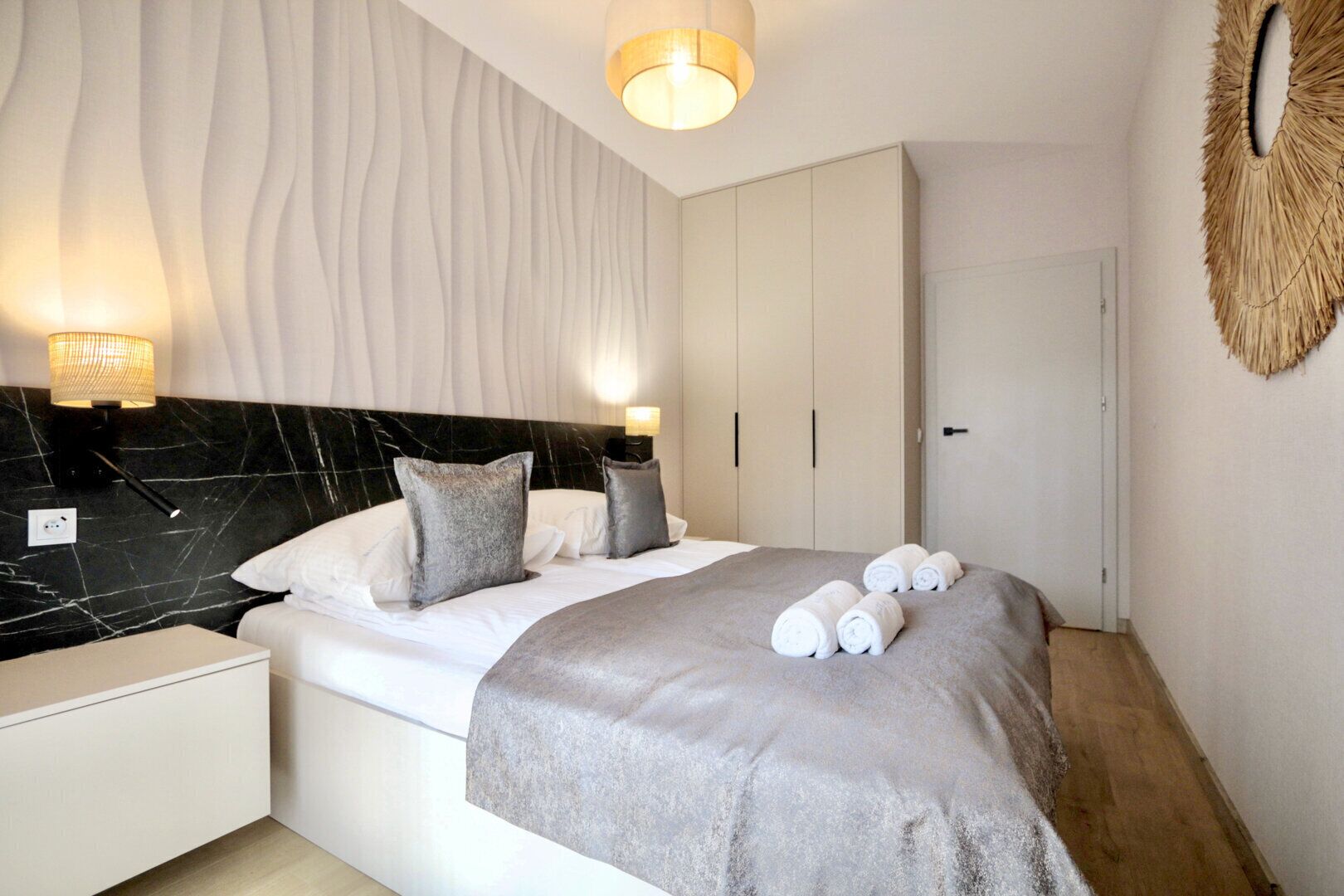 Une chambre d’hôtel moderne comprenant un lit, des tables de chevet, une tête de lit en marbre et une armoire.