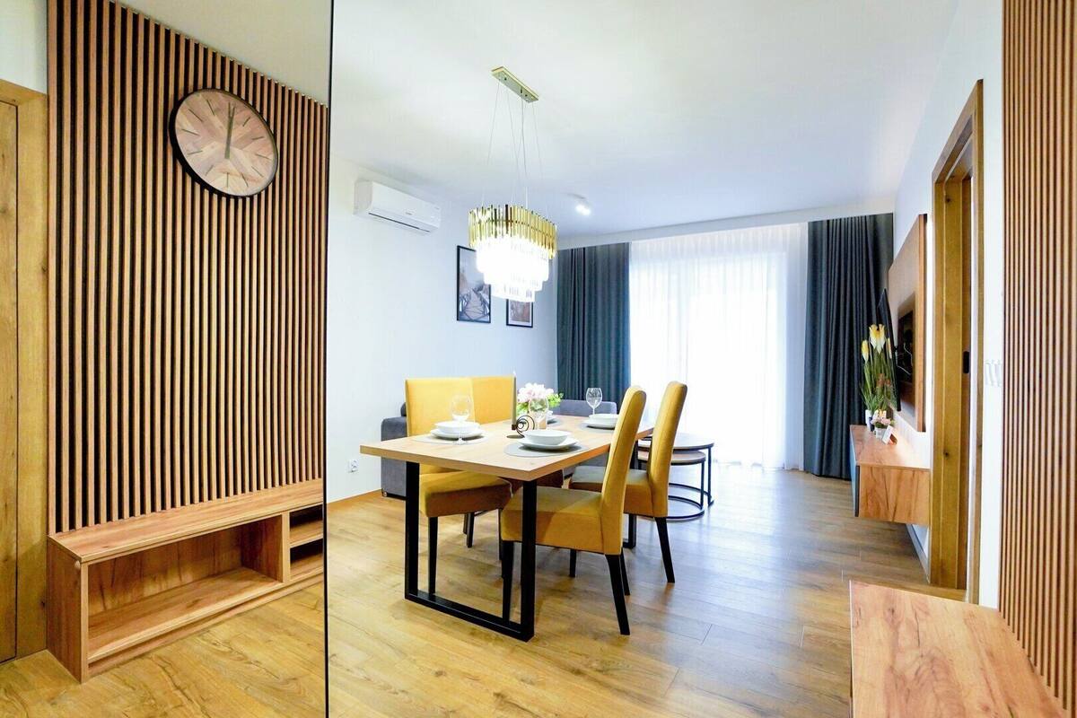 A modern dining area with a wooden wall, a round clock, and a chandelier.