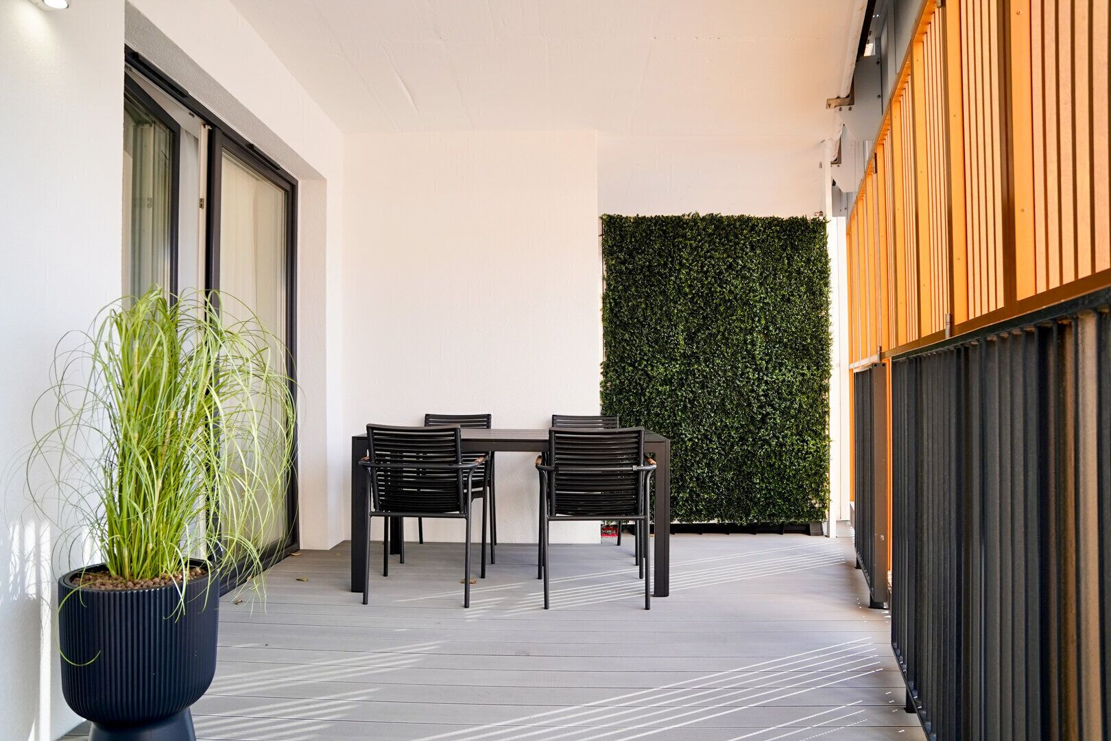 A modern outdoor patio with a table and chairs, a potted plant, and a vertical garden wall.