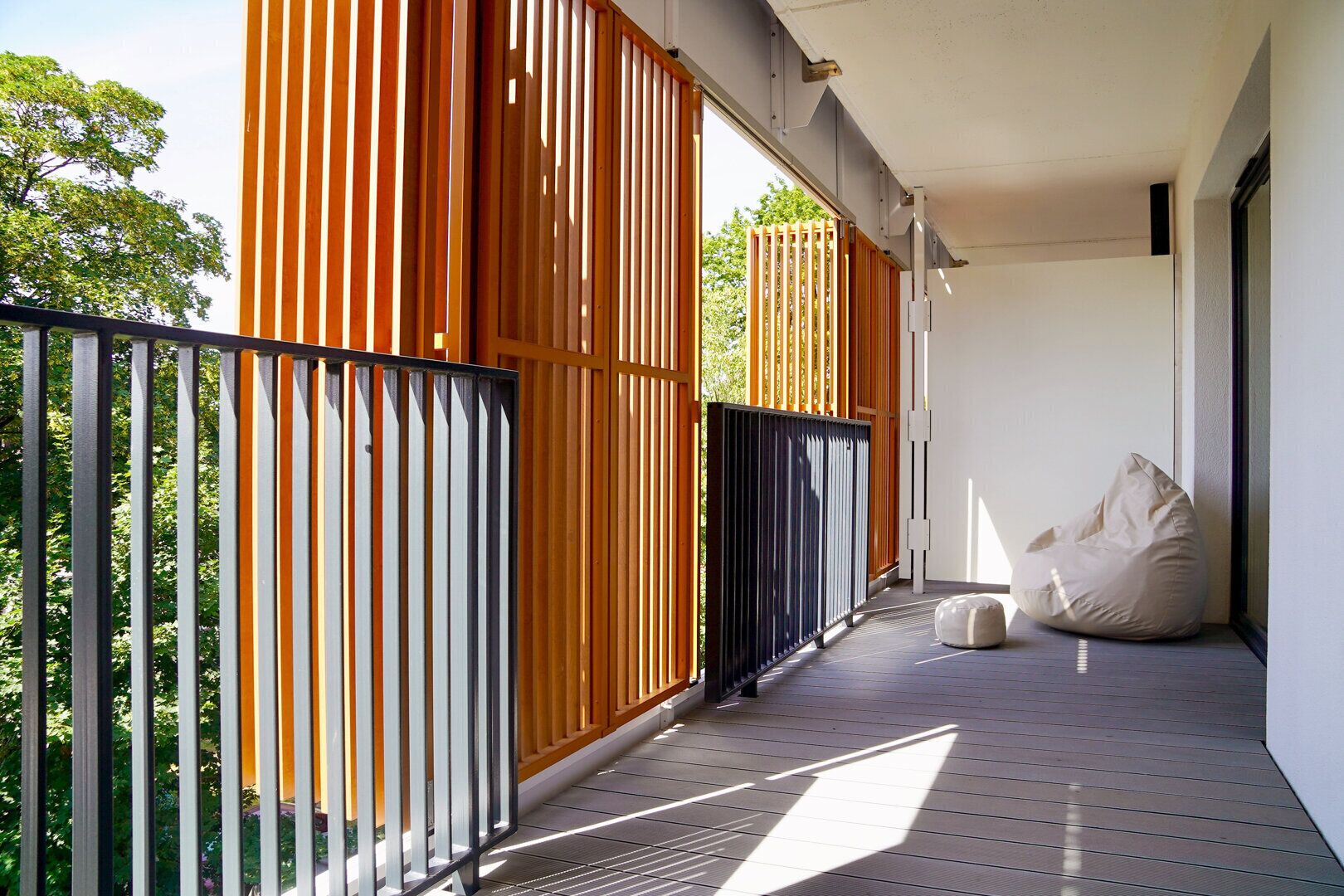 Un balcón con cerca de madera, un sillón informal de rafia y vistas a árboles.