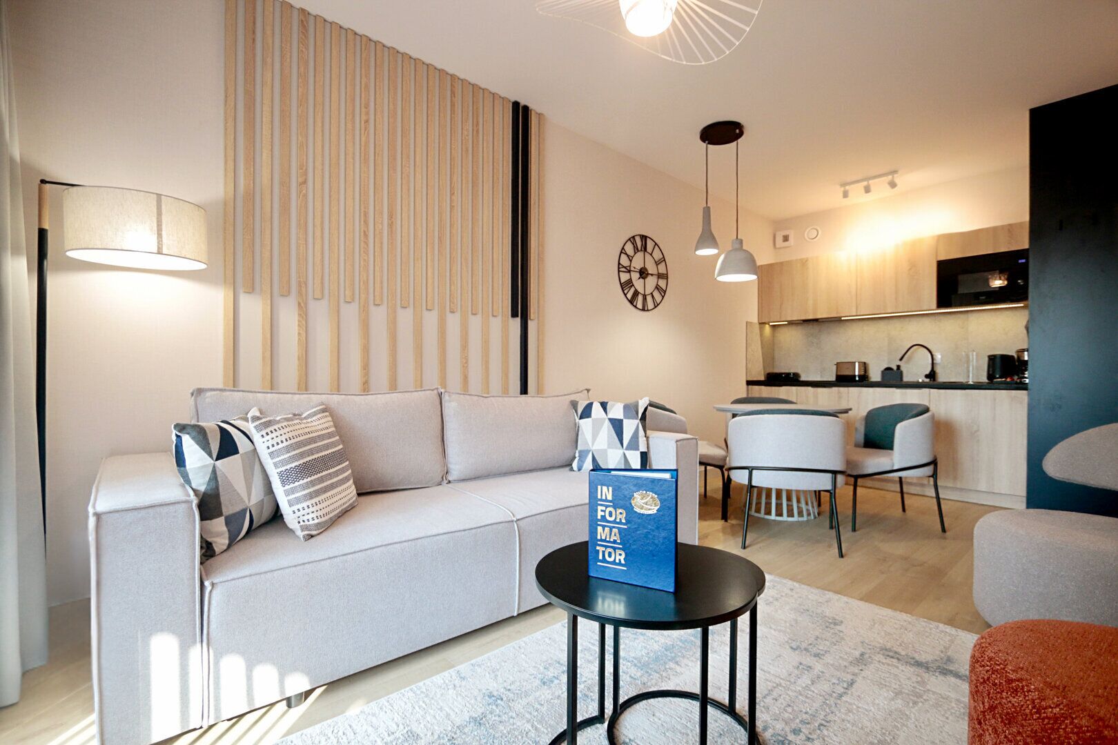 A modern living room with a sofa, a coffee table, and a dining area with chairs. There is a kitchen in the background.