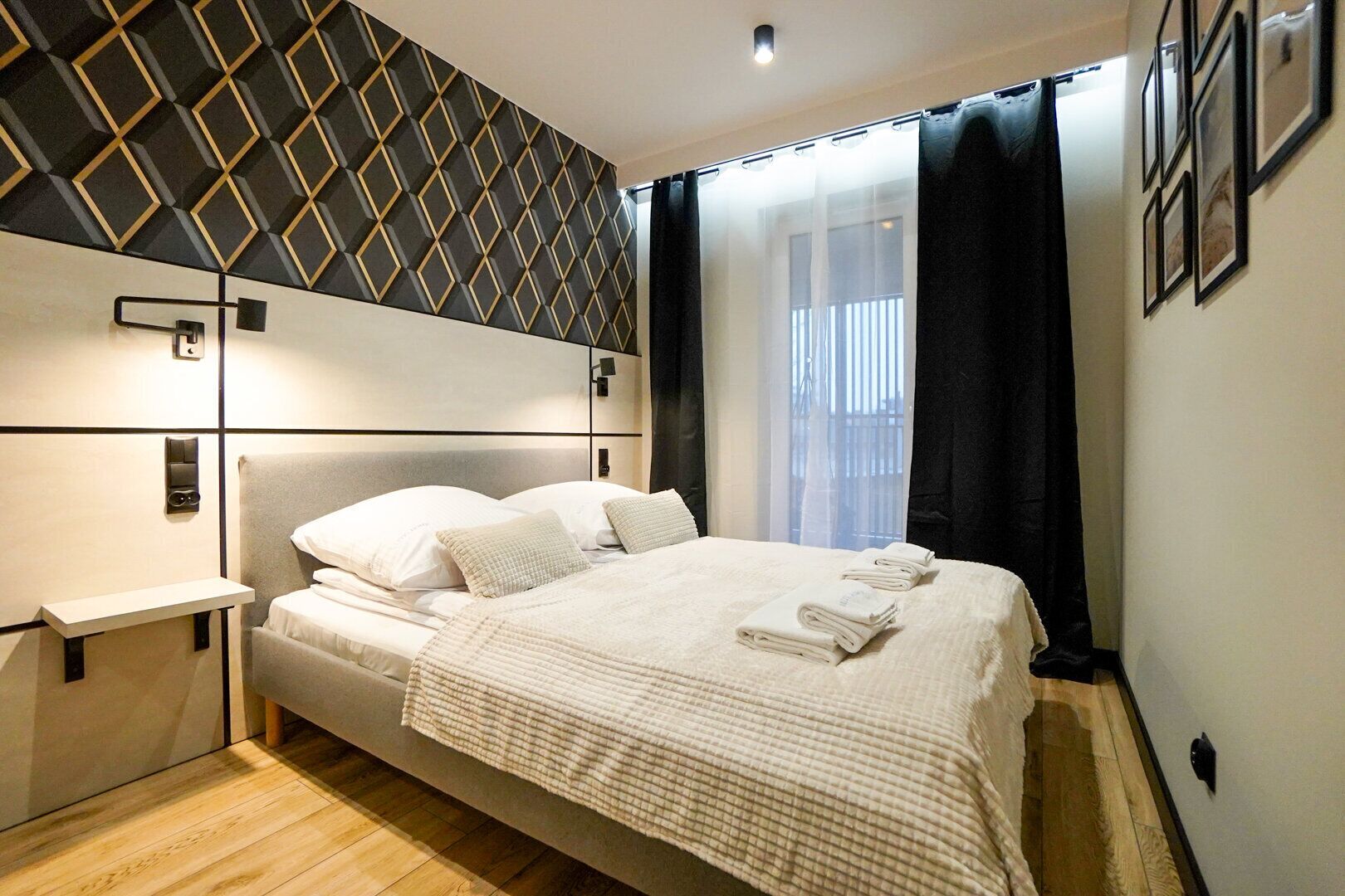 Ein modernes Hotelzimmer mit einem großen Bett, einem Nachttisch, einer Wandleuchte und einem Fenster mit Vorhängen.