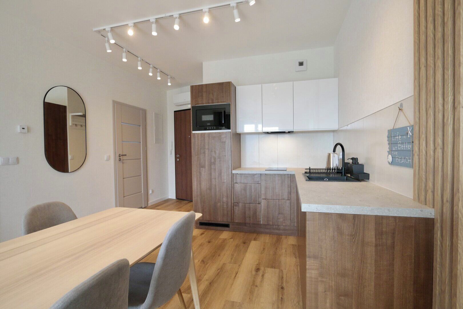 A modern kitchen with a wooden island, white cabinets, and a built-in microwave. There is a dining area with a table and chairs, and a mirror on the wall.