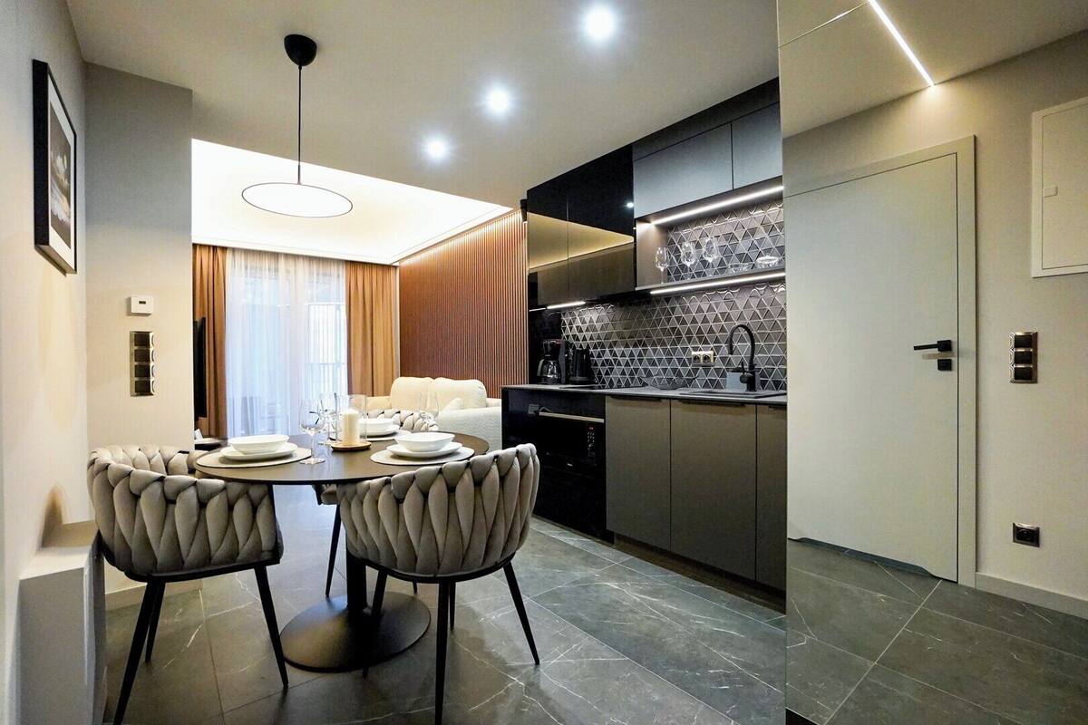 A modern kitchen with a dining area, featuring a round table with chairs, a built-in oven, and a tiled backsplash.