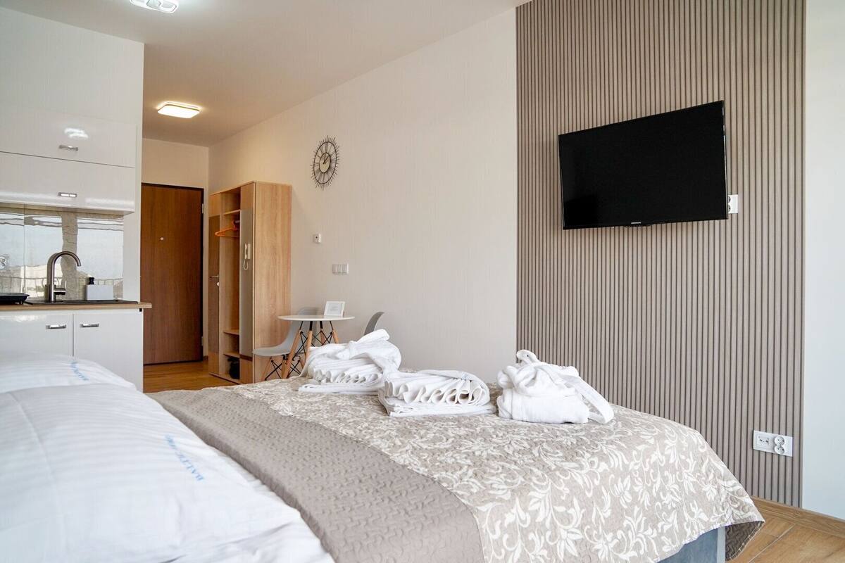 A hotel room with a bed, a TV mounted on the wall, a small table with a chair, and a bathroom visible through an open door.