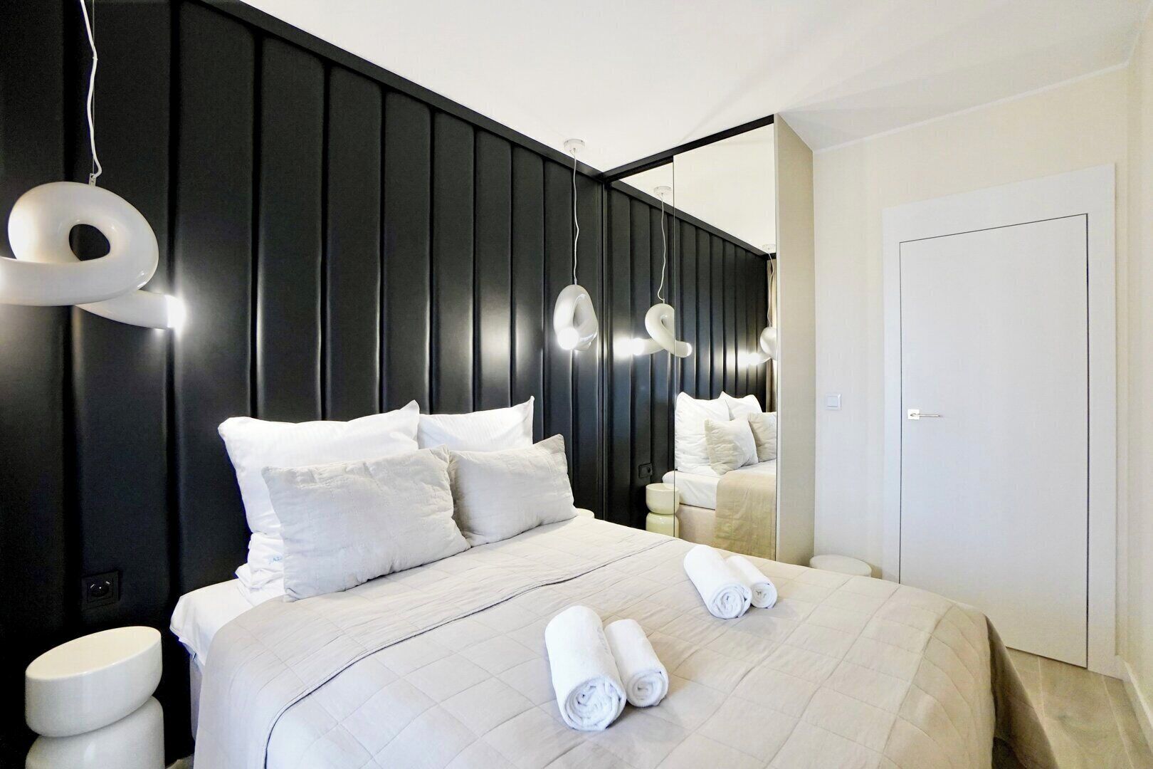 A modern hotel room with a large bed, white bedding, and a black accent wall.