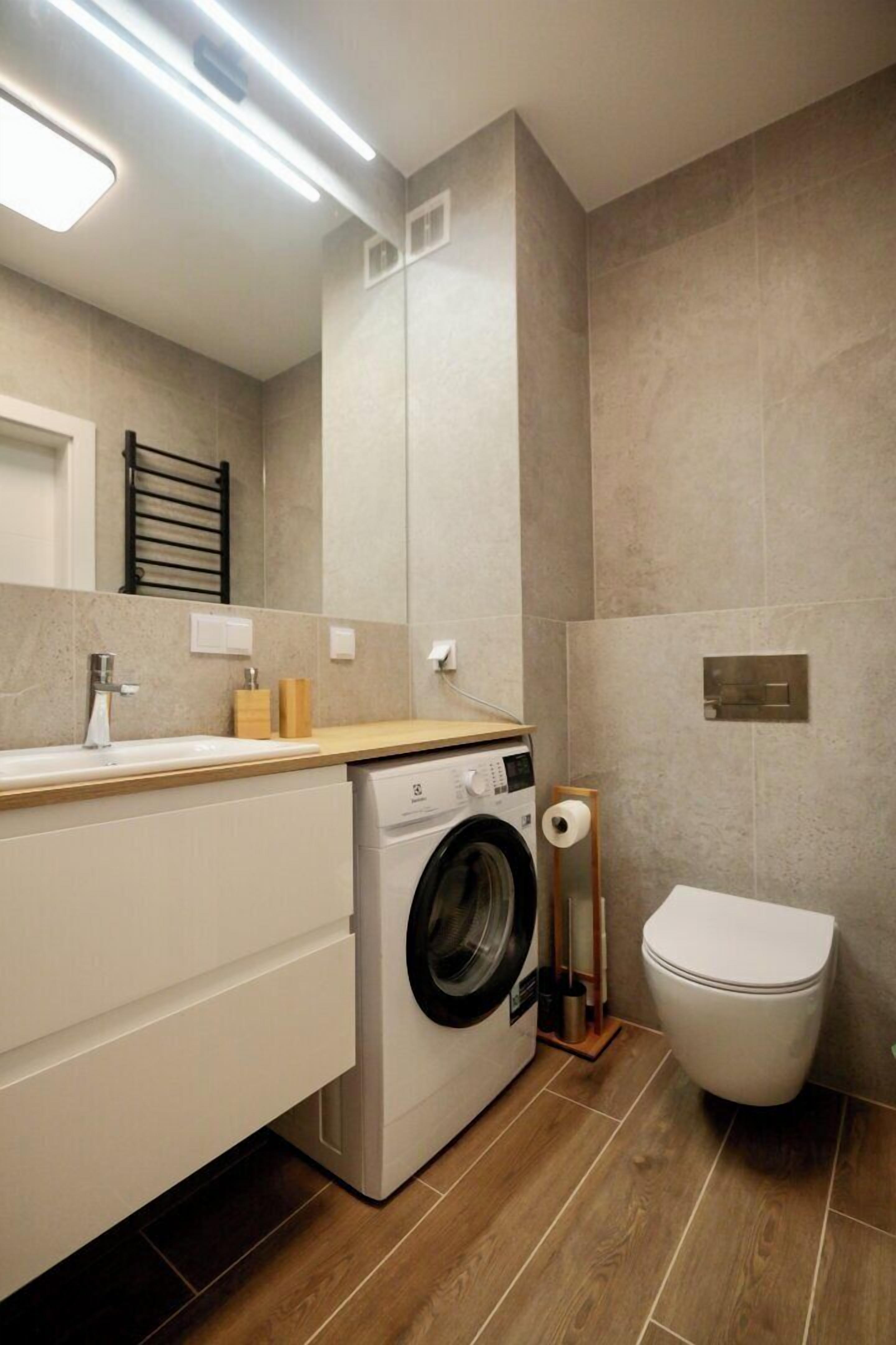 A modern bathroom with a washing machine, toilet, and a wooden vanity.