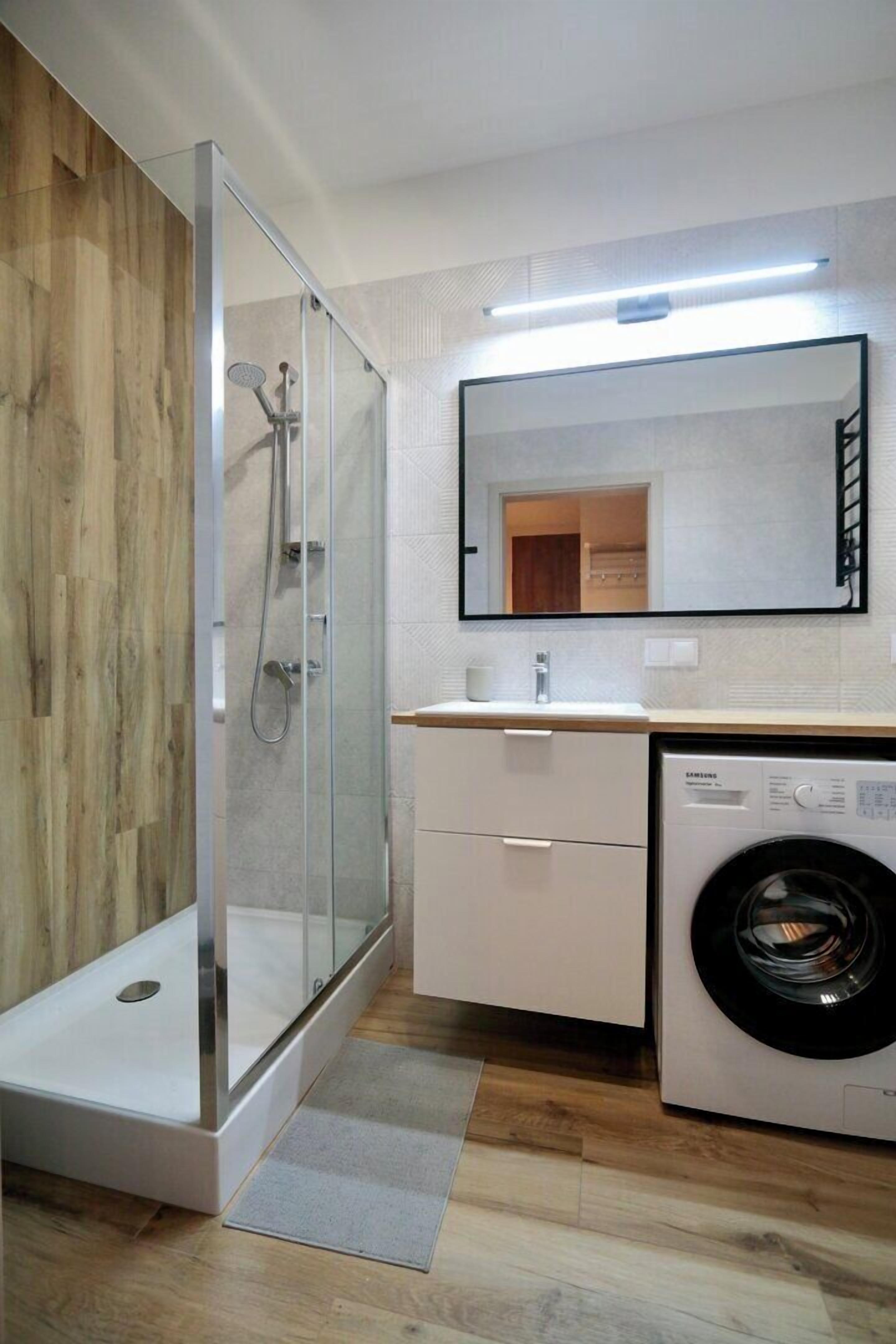 A modern bathroom with a glass-enclosed shower, a built-in washing machine, and a large mirror above the sink.