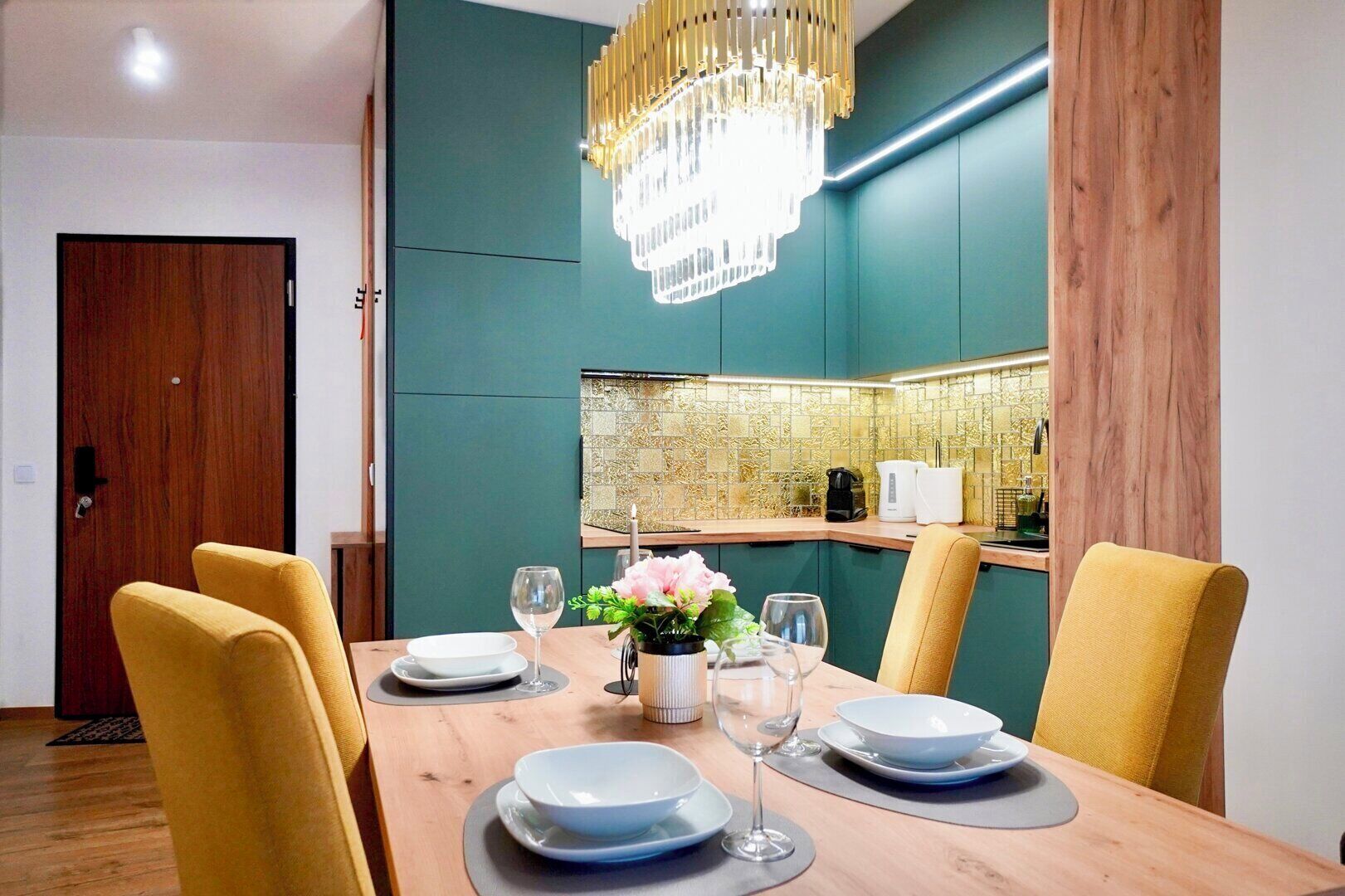 A dining area with a wooden table set for four, a chandelier, and teal walls.