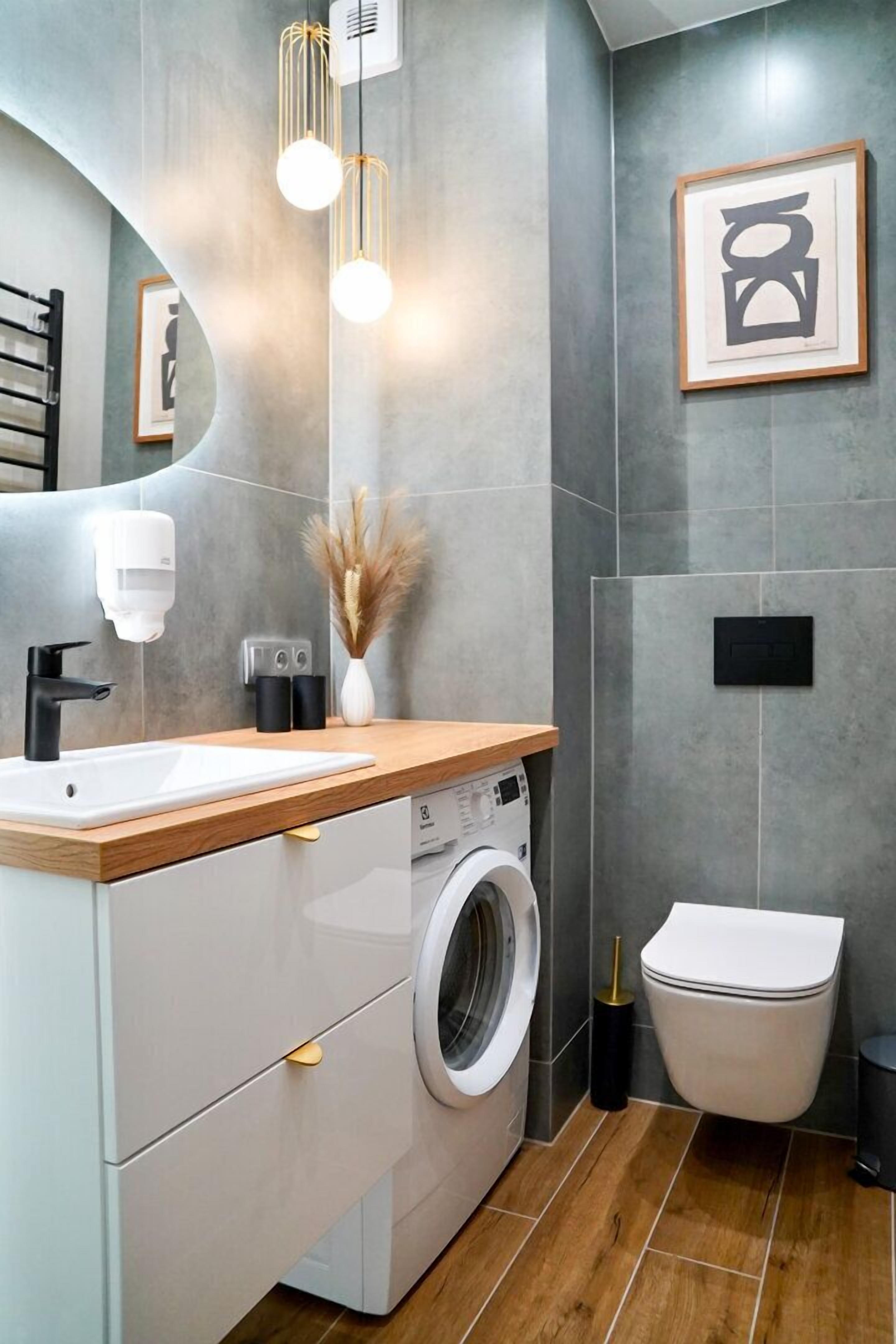 Une salle de bain moderne avec un meuble-lavabo en bois, un lave-linge, des toilettes et une œuvre d’art encadrée au mur.