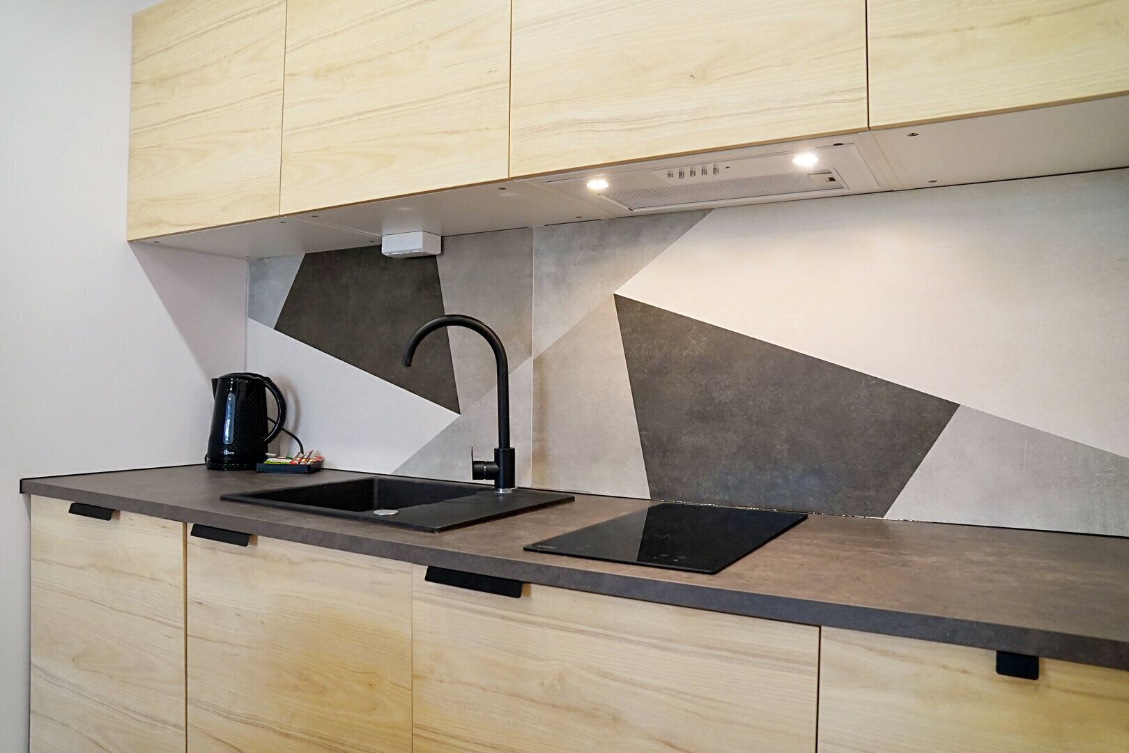 Eine moderne Küche mit zwei schwarzen Spülen, Holzschränken und einer geometrischen Spritzschutzwand.
